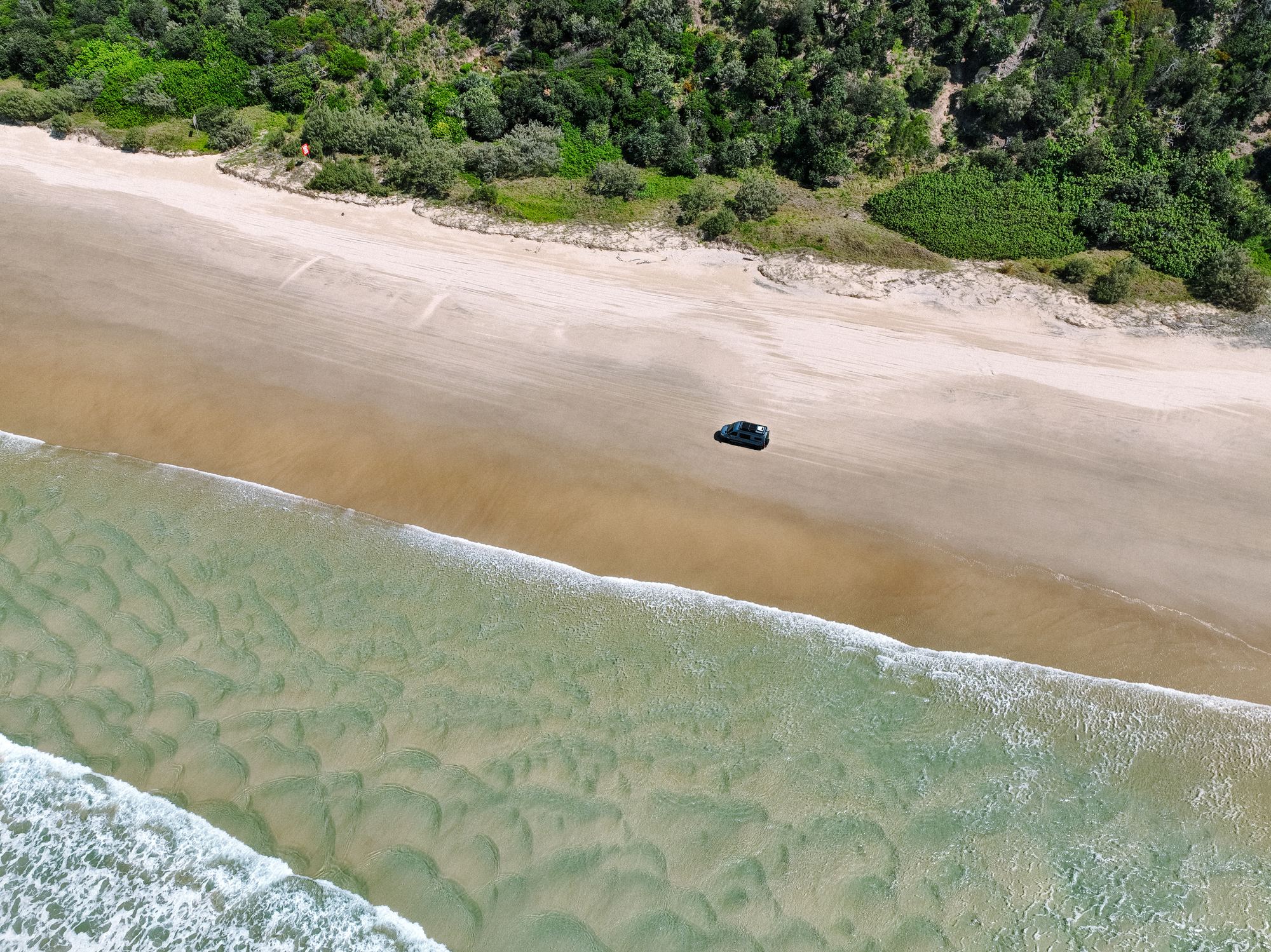 Aerial view of a Hinter Vans Sprinter driving along an empty beach